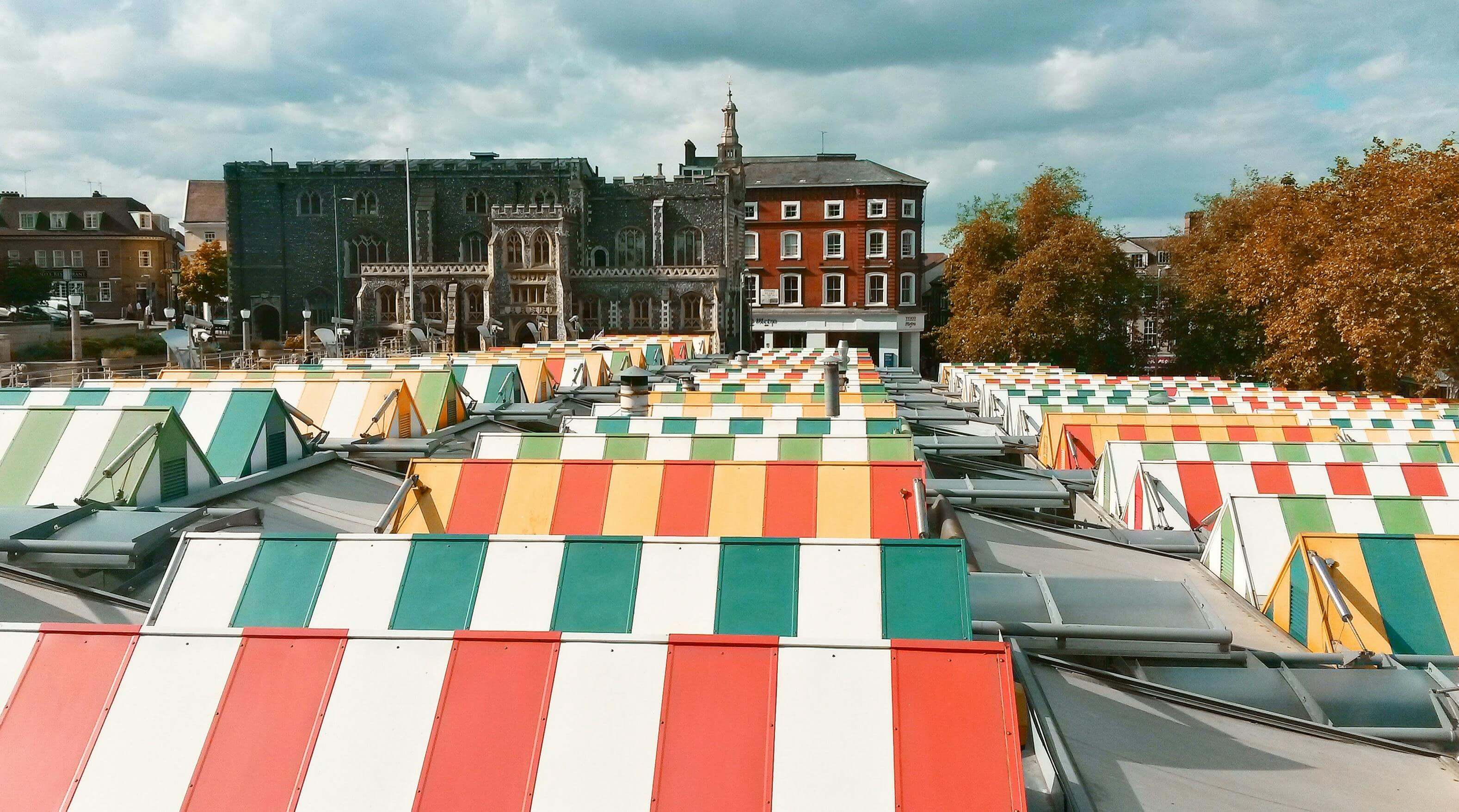Colourful striped awnings of Norwich Market stalls with Guildhall behind